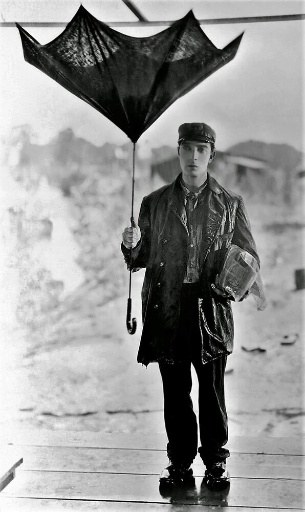 Buster Keaton, impassible, tenant un parapluie retourné sous la pluie